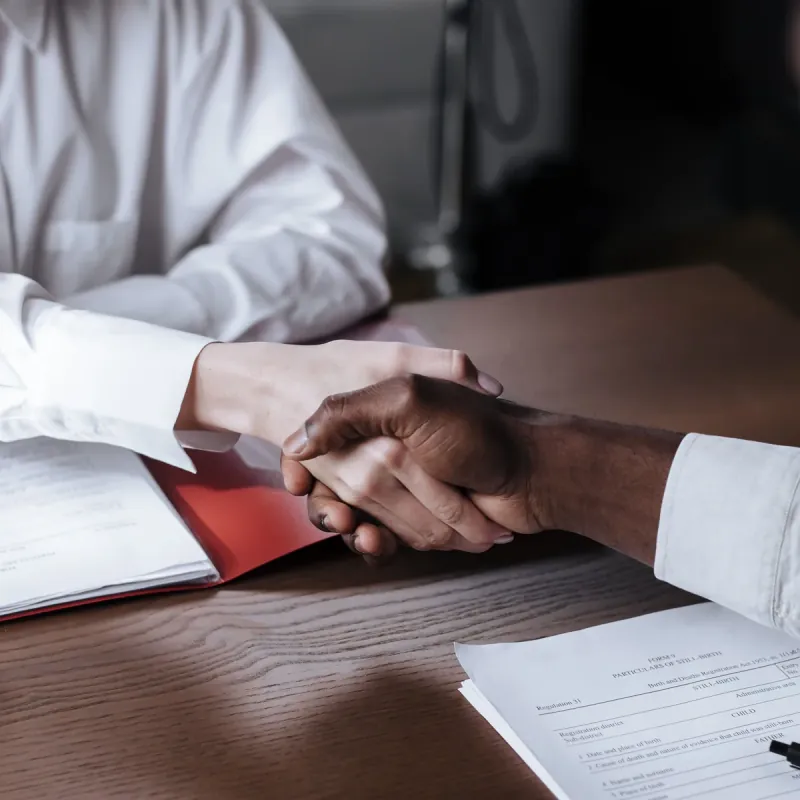 Dos personas se dan la mano sobre una mesa con documentos.